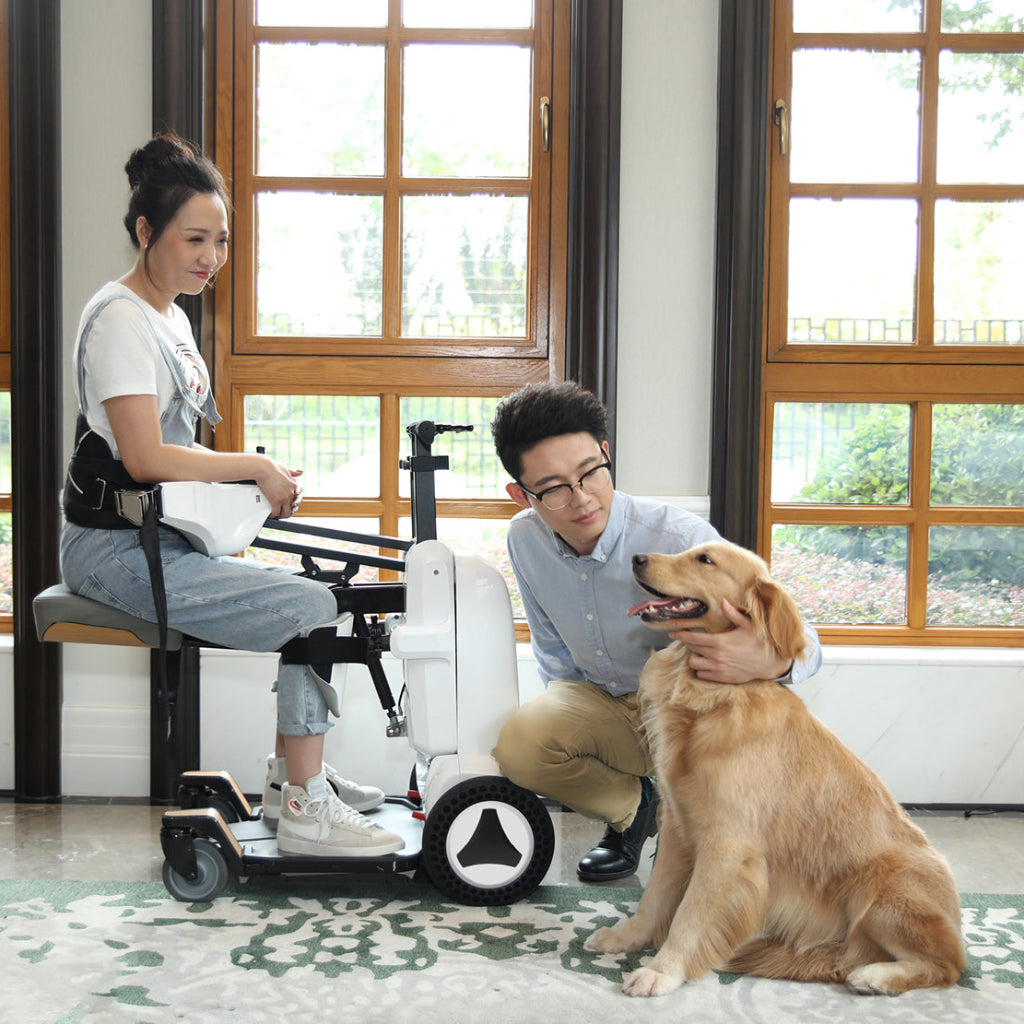 Woman using a mobility scooter with a man and a dog in a room with large windows.